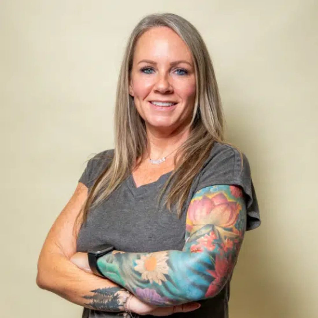 Smiling woman with tattooed arm in gray shirt against beige wall