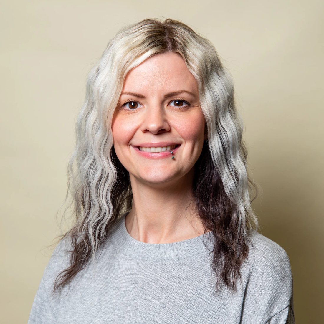 Woman with wavy gray hair in gray sweater smiling