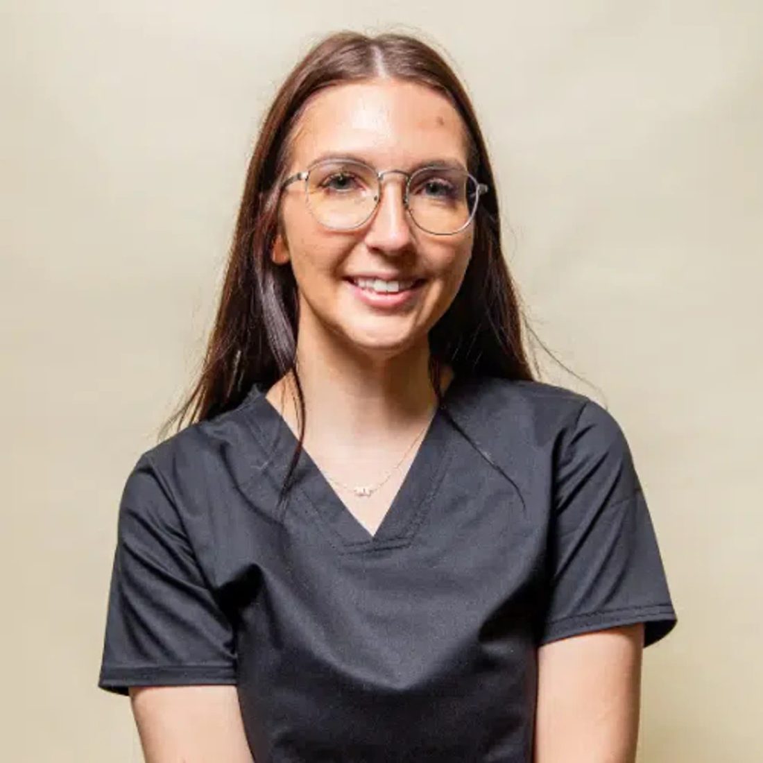Young woman with glasses in black scrubs smiling at camera